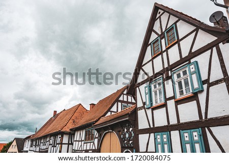 Old town in Germany. Small half timbered houses. Very old ancient houses made out of wood with ornate decorations and colors. Grey blue sovercast sky and green trees. Small windows and angled roofs.