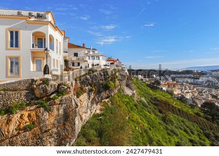 Old town of Nazare city and crumbling mountain slope. Dangerously hanging houses and pedestrian path on the steep cliff over the modern city of Nazare, Portugal.