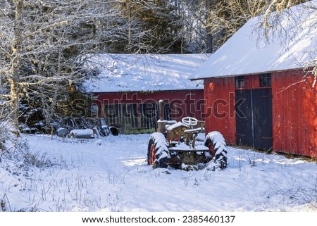 Old tractor by red barns on a cold winter day