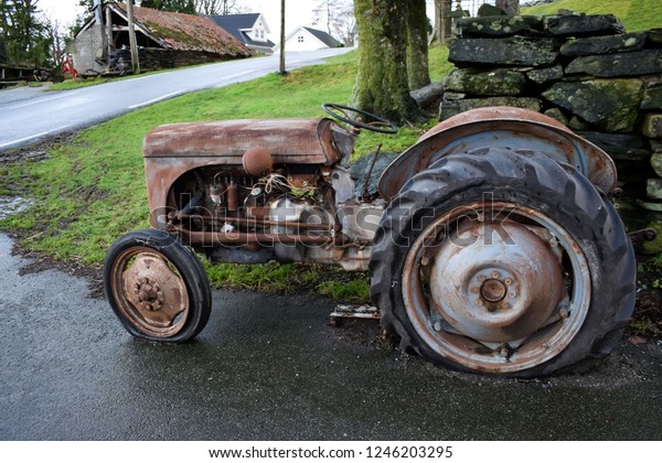 An old tractor stands on the side of the road.\
The tractor is covered with\
rust.