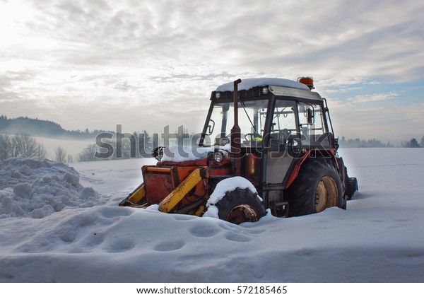 Old tractor under the snow. Snow calamity in\
transport. Frozen diesel\
engine.