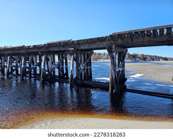 An old train bridge stretching across water at low tide on a winter day.