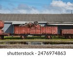 Old train cargo wagons rusting in an industrial yard, car wreck loaded on top