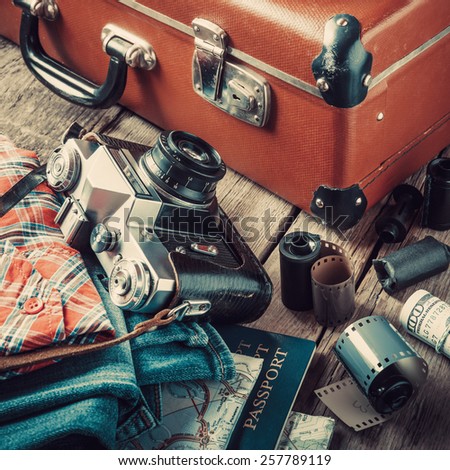 Old travel suitcase, sneakers, clothing, map, filmstrip and retro film camera on wooden background. Vintage stylized.