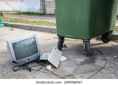 Old tube television and other electronics, such as an old keyboard on the street pavement next to a green dumpster. Concept of recycling technology - Shutterstock ID 2090586967