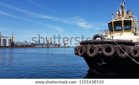 Old tugboat mooring in maritime port with calm blue water. Marine port industrial seascape. Used black tires at shipboard of tug