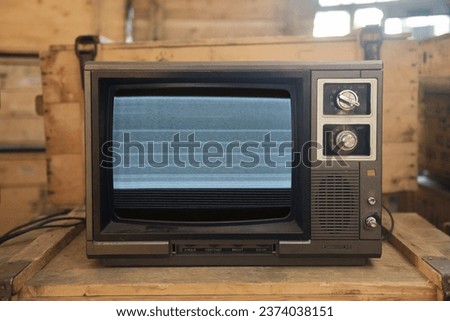 An old TV with noise on the screen sits on a box.
