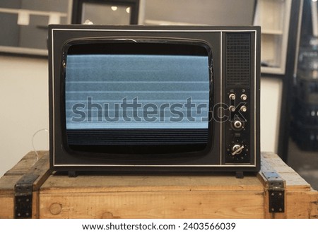An old TV with noise on the screen sits on a box.