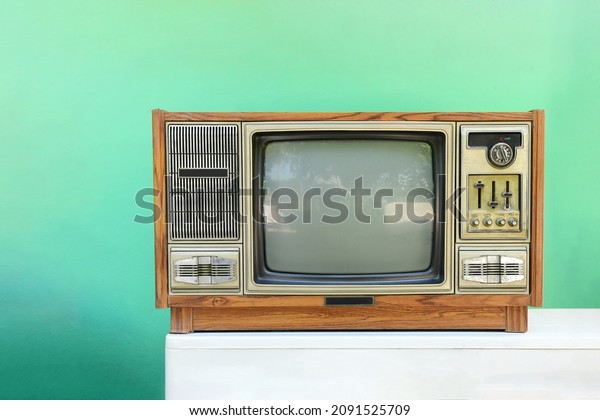 Old TV\
vintage, tv tube television in wood case on white table green wall\
background tv electric home use\
equipment.