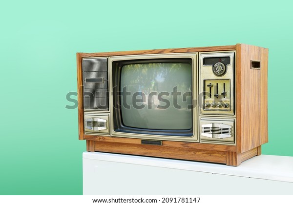 Old TV\
vintage, tv tube television in wood case on white table green wall\
background tv electric home use\
equipment.