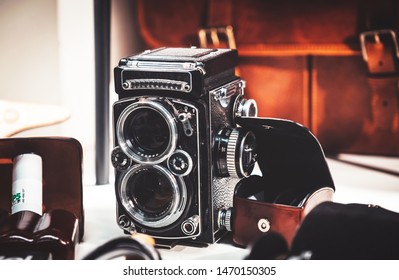Old twin lens reflex camera and leather equipment in front of the brown leather handbag. Gentleman style photography.
					Analog photography machine.
					
					