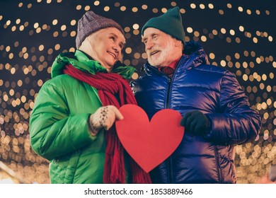 Old Two People Parents Married Couple Man Woman Have Date On X-mas Christmas Midnight Walk Hold Red Paper Card Heart Under Garland Illumination Outside Wear Coat Scarf Hat