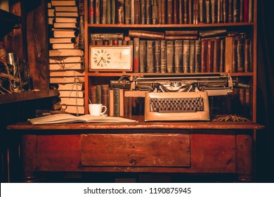 Old Typewriter Is On The Table Next To The Book Lies And Is A Cup.old Books Are On The Shelves.Vintage Room Of The Researcher, Critic, Scientist,