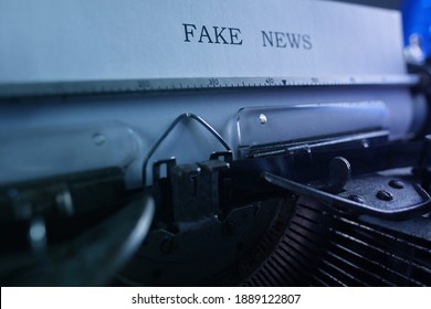 old typewriter on table, words fake news printed on paper in large size, candle is burning, retro style, concept of information hoax in social media, misleading, exposing deception, selective focus