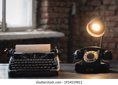 Old typewriter, rotary phone and lamp on the retro desk table background.