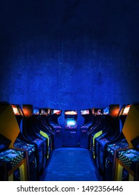 Old Unbranded Vintage Arcade Video Games In A Dark Gaming Room With Blue Light With Glowing Displays And Concrete Wall - Vertical Photo Of Retro Design With Free Copy Space For A Poster Or Magazine