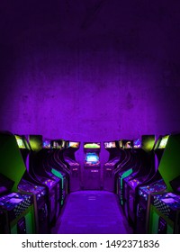 Old Unbranded Vintage Arcade Video Games In A Dark Gaming Room With Purple Light With Glowing Displays And Concrete Wall - Vertical Photo Of Retro Design With Free Copy Space For A Poster Or Magazine