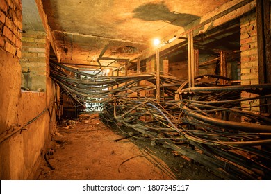 An old underground brickwork cable tunnel or basement with cables with tungsten lamp lighting. Underground space with optical cables for internet, television and telephone.
