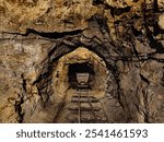 Old underground mine tunnel, mining cart and tracks. Rocky, narrow mine passage