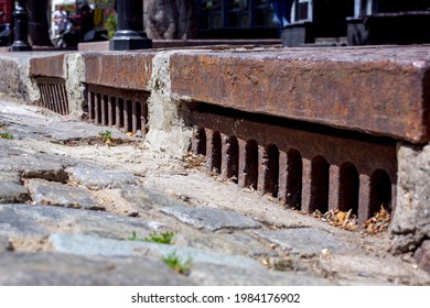 Old Urban Infrastructure Drainage System With Rusty Iron Grating Stormwater System Road At The Curb Close-up.