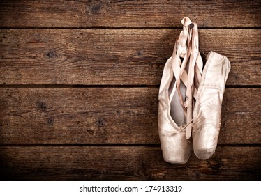Old used pink ballet shoes hanging on wooden background