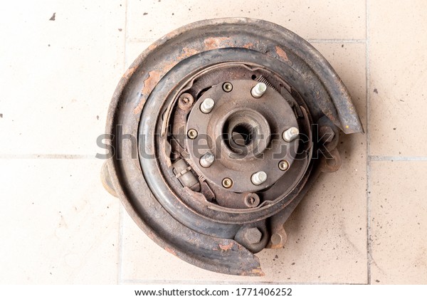 Old, used, rusty rear hub, on which the brake\
pads of the parking brake are visible, without brake disc on the\
beige tiled floor of the\
workshop