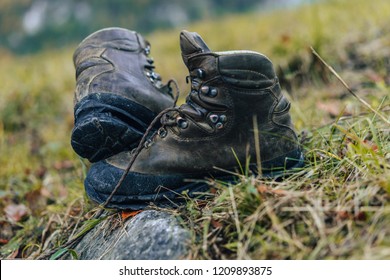 Old Used Trekking Shoes On Grass. Dirty Boots With Laces, Leather Shoe, Old And Broken. Walking Or Hiking Shoes On A Stone, Grass And Rock.