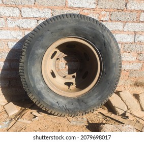 an old and used up truck tire with no air and covered in dust and rust is resting outside against a concrete wall surrounded by rubble and dirt
