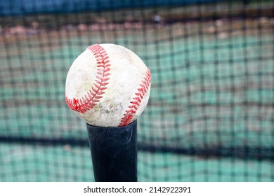 A Old Used Worn Baseball Sitting On A Batting Practice Tee