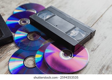 Old VHS cassettes rest on scratched compact discs, creating a contrast between different generations of information storage. The photo conveys an atmosphere of nostalgia for the times of VHS and CDs.