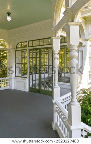 Old Victorian house front porch with white wooden railings, supports and arches.