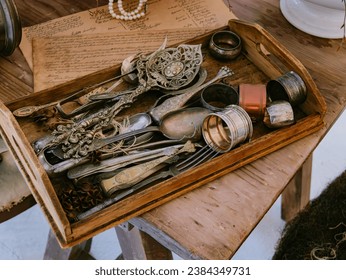 Old Victorian-era silverware, forks and spoons, and other utensils sitting in a tray, on top of some old mail letters in a vintage antique shop - Powered by Shutterstock