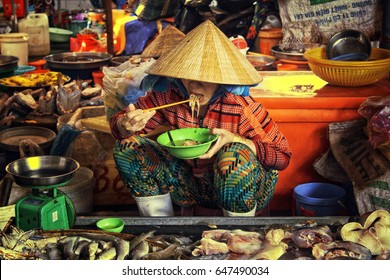 Old Vietnamese woman sitting on a fruit floating market in Ha tien and eating her rice noodles