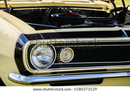 old vintage American muscle cream white car half front, left side, open hood engine parts view, close up on headlights light lamp, chrome bumper