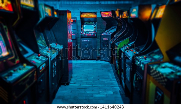 Old Vintage Arcade Video Games in an empty dark\
gaming room with blue light with glowing displays and beautiful\
retro design