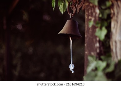 An Old Vintage Bell Outdoor The House. Rusty Metal Texture On Black Background. Traditional Garden Decorative Object. A Rustic Dark Brown Bronze Doorbell With A White Rope.