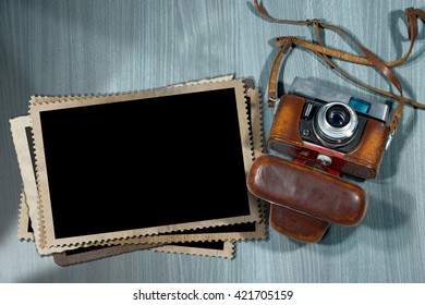 Old and vintage camera with leather case and a stack of photo frames on a desk with shadows