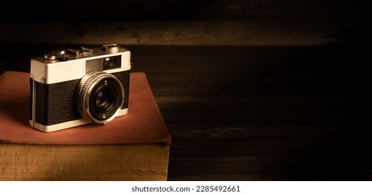 Old vintage camera  on a rustic table against a low light warm  dark background - low light under exposed photography - selective focus - Powered by Shutterstock