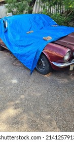 Old Vintage Car Covered Up By Blue Cover Held By Bricks