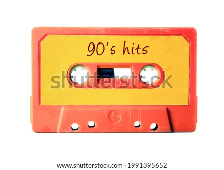 An old vintage cassette tape (obsolete music technology) with the handwritten text: 90's hits. Light red plastic body, vivid orange label, isolated on white.
