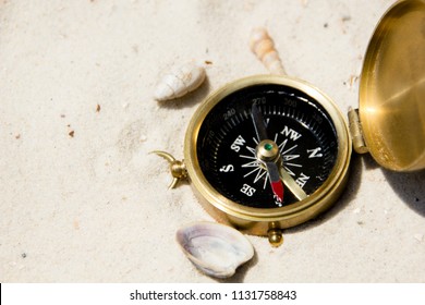 An old and vintage compass in the sand of a beach surrounded with shells leading to new adventures or guiding the way and path to go to. It is a methaphor for leadership or guidance also. - Shutterstock ID 1131758843