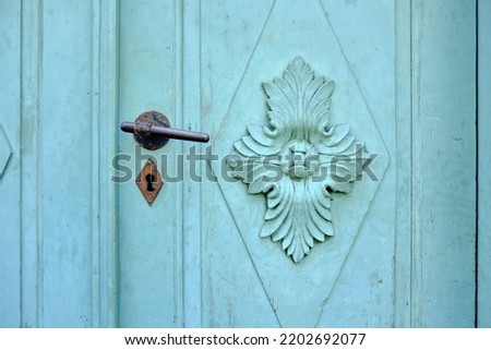 Old vintage door hardware on a green door with ornate coffered panel.