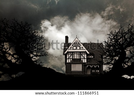 An old vintage eerie haunted house with creepy gnarly dead trees against a apocalyptic dark sky for Halloween concept.