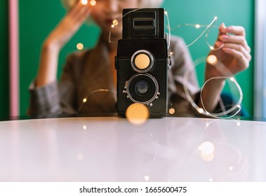 Old Vintage Film Two Lens Camera Surrounded By Fairy Lights With The Blurred Female Silhoutte In The Back, Selective Focus