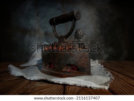 An old vintage iron iron with coals inside and steam on a wooden table with a linen napkin.