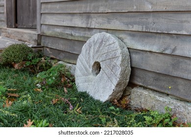 Old Vintage Mill Has A Replica Millstone Grinding Stone Leaning Against The Old Wood Siding Of The Buidling.