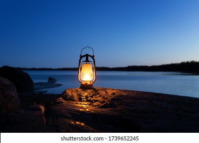 An old vintage oil lantern on a rock by the sea. Evening time. Beautiful colorful illuminated lamp. Chillout travel concept. 