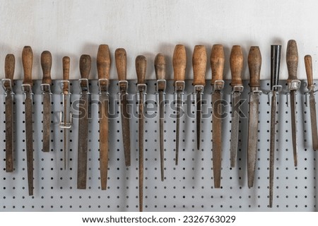 Old vintage rasps with wooden handles hanging on steel wall as background. A set of files and rasps for hand sanding, close up. Hand work tool in workshop