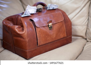 Old vintage red leather case full of money coming out of the sides. Scratched bag on leather sofa, business, bribe or prize concept. Indoors, copy space.