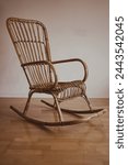 An old vintage rocking chair made of bamboo or rattan in boho style in front of a white wall.